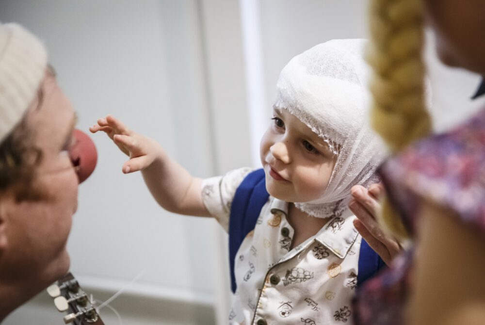 Enfant avec bandage à la tête essaynt d'attraper le nez rouge d'un clown