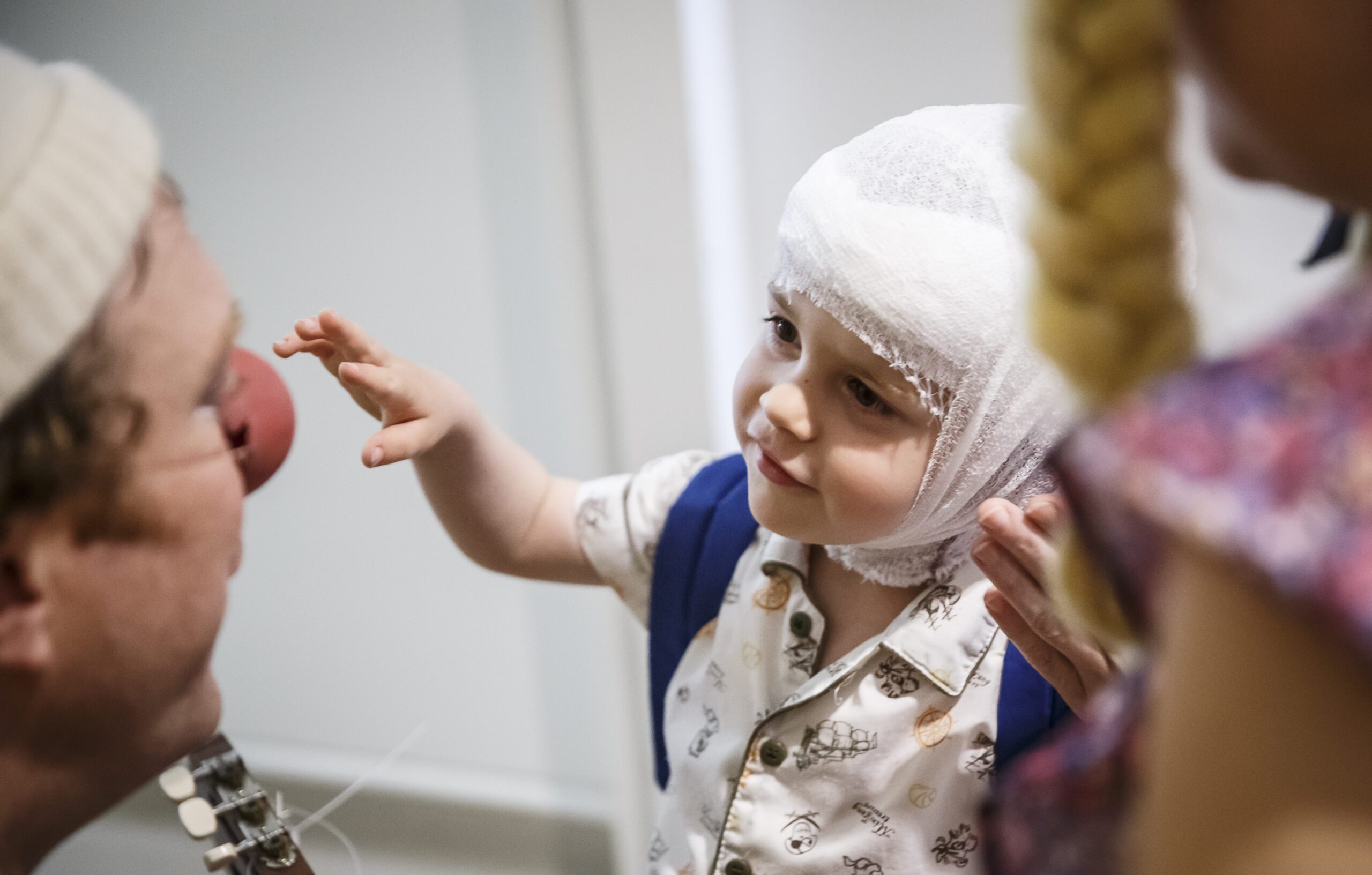 Enfant avec bandage à la tête essaynt d'attraper le nez rouge d'un clown